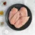 Three raw chicken breasts on a black plate, next to small glass bowls containing various spices and seasonings, on a light-colored surface.