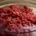 A clear glass bowl filled with raw ground beef, shown in close-up on a neutral background.