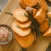 Sliced sweet potatoes on a wooden cutting board with sprigs of rosemary and a small bowl of coarse pink salt on the side.