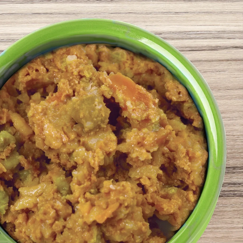 A green bowl filled with chunky, orange and green vegetable curry sits on a wooden surface.