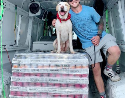 Young man and cute dog sitting on top of a lot of canned dog food for shelter pets